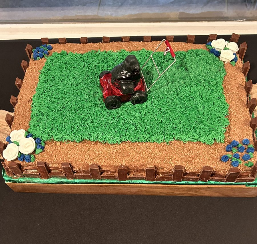 Groom's cake shaped like a fenced green lawn with a red lawn mower